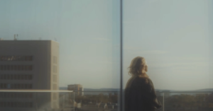 woman stands at a window looking at the skyline. Dynamic glass solutions allow for easy variation in glass states, offering a unique look and feel to your architectural project