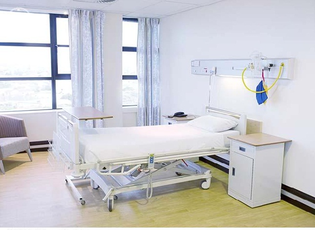a standard hospital bed with a light switched on attached to the headboard